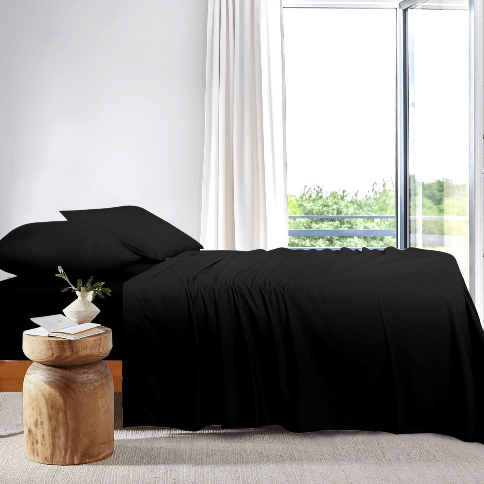Side view of a neatly made bed dressed in black bamboo sheets next to a large window in a bright bedroom