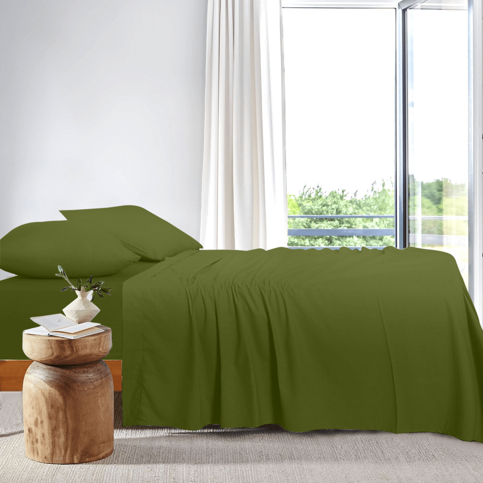 Side view of a neatly made bed dressed in olive green bamboo sheets placed next to a bright window.