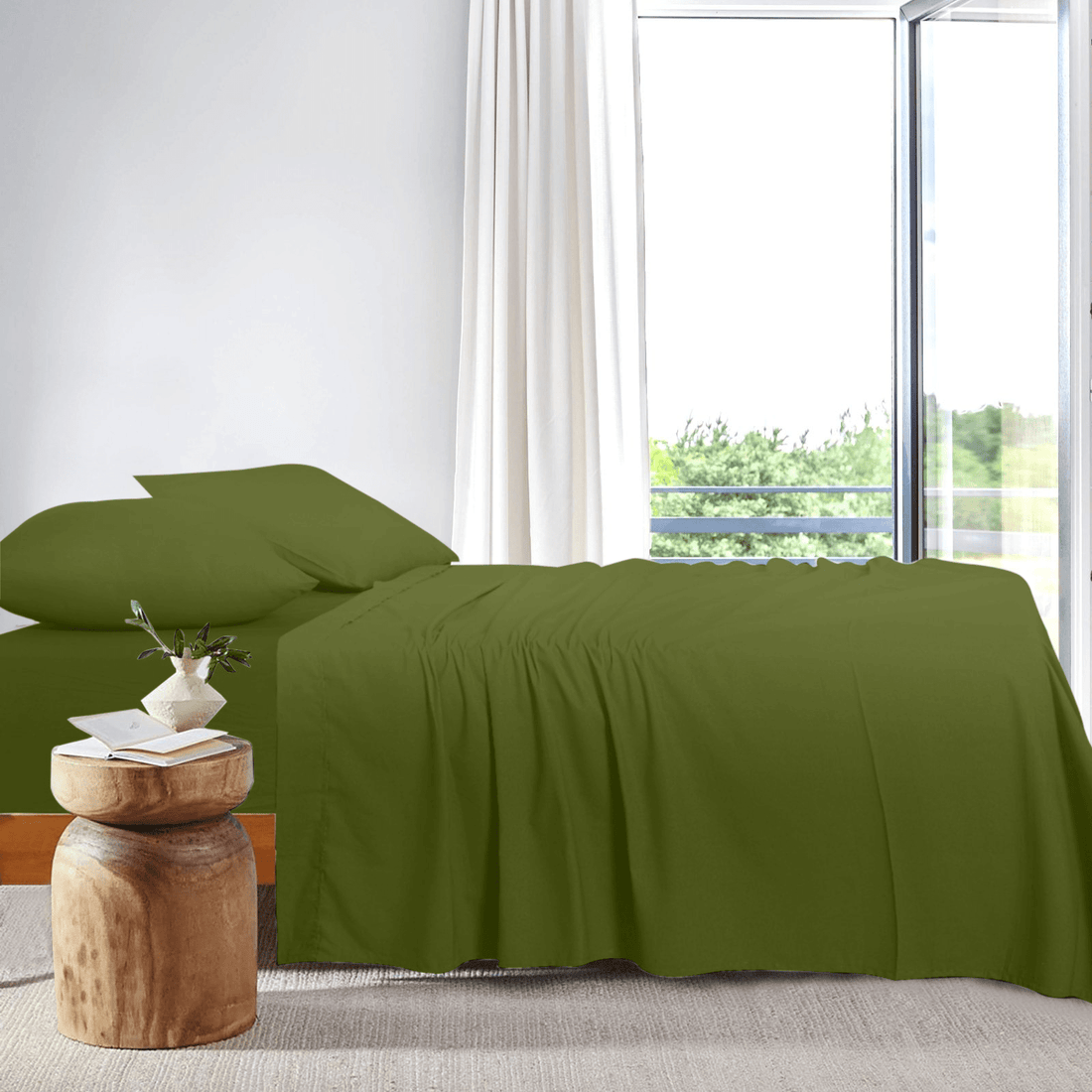 Side view of a neatly made bed dressed in olive green bamboo sheets placed next to a bright window.