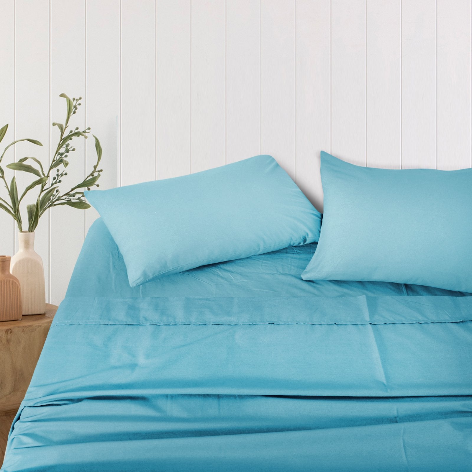 Pair of solid teal bamboo pillowcases arranged neatly on a bed against a white wood-paneled wall