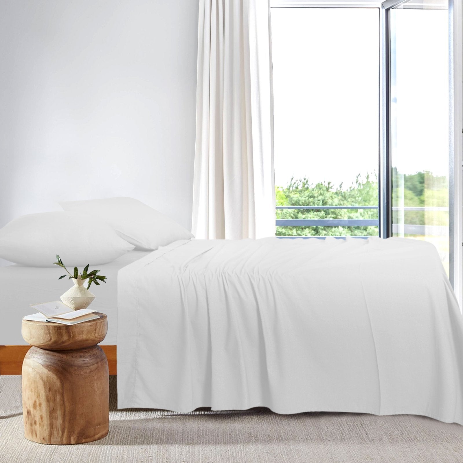 Side view of a bright modern bed dressed in crisp white bamboo sheets placed next to a sunlit window