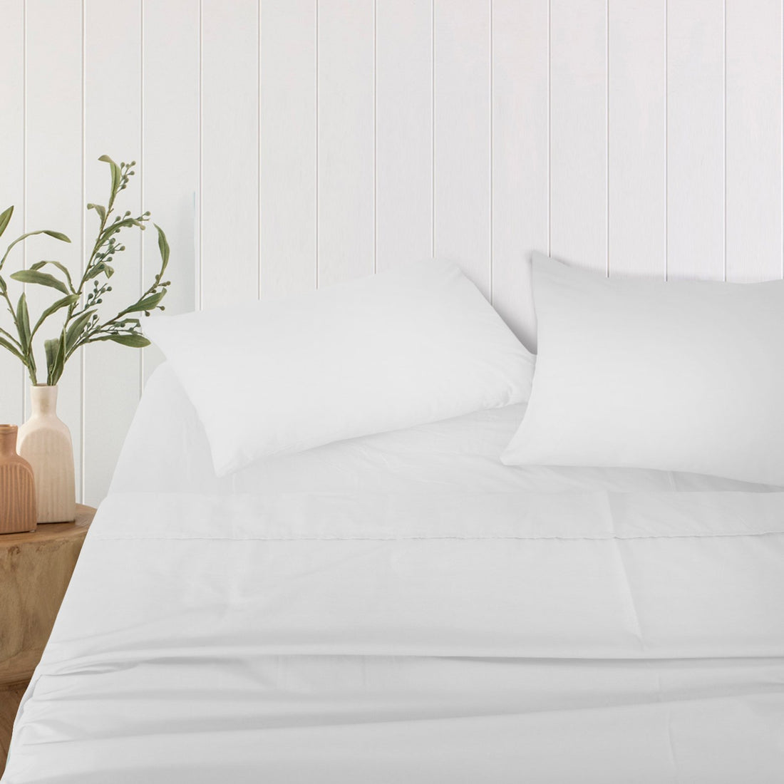 Pair of pure white bamboo pillowcases arranged neatly on a bed against a white wood-paneled wall.