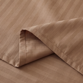 Side angle of stacked brown striped cotton rich pillows styled on a luxury bed