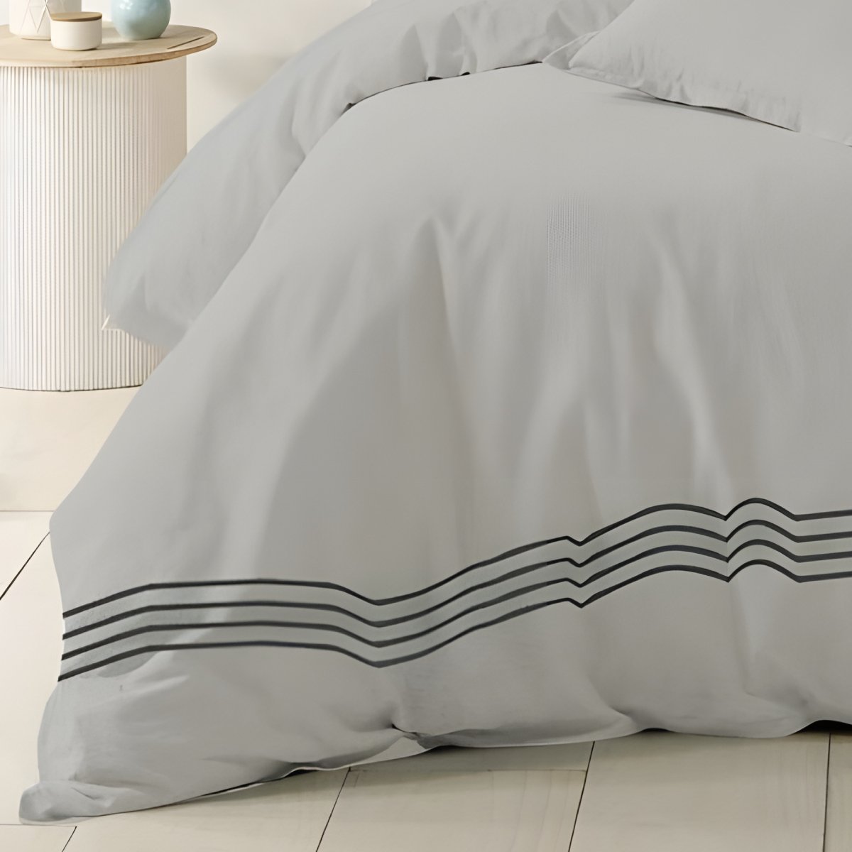 Silver cotton quilt cover styled with blue cushions in a bright bedroom.