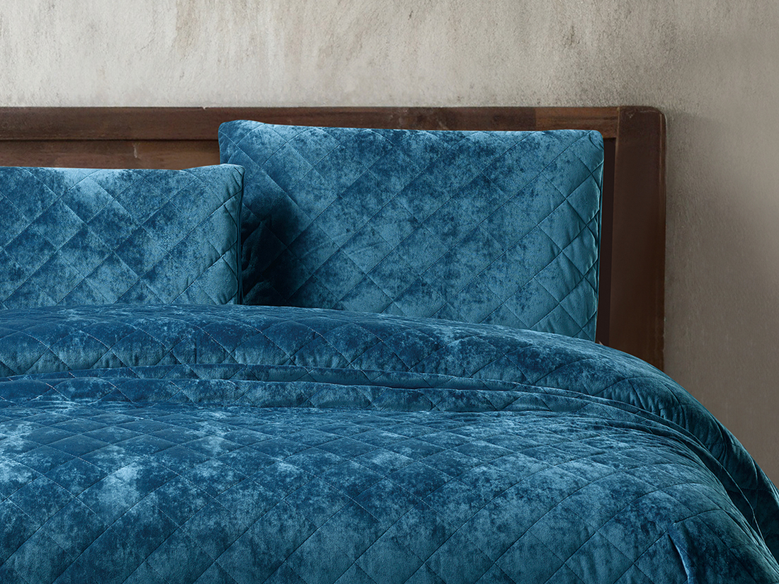 Deep teal velvet bedding with matching diamond-patterned pillows on a wooden bed.