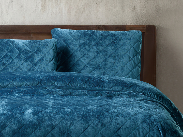 Deep teal velvet bedding with matching diamond-patterned pillows on a wooden bed.