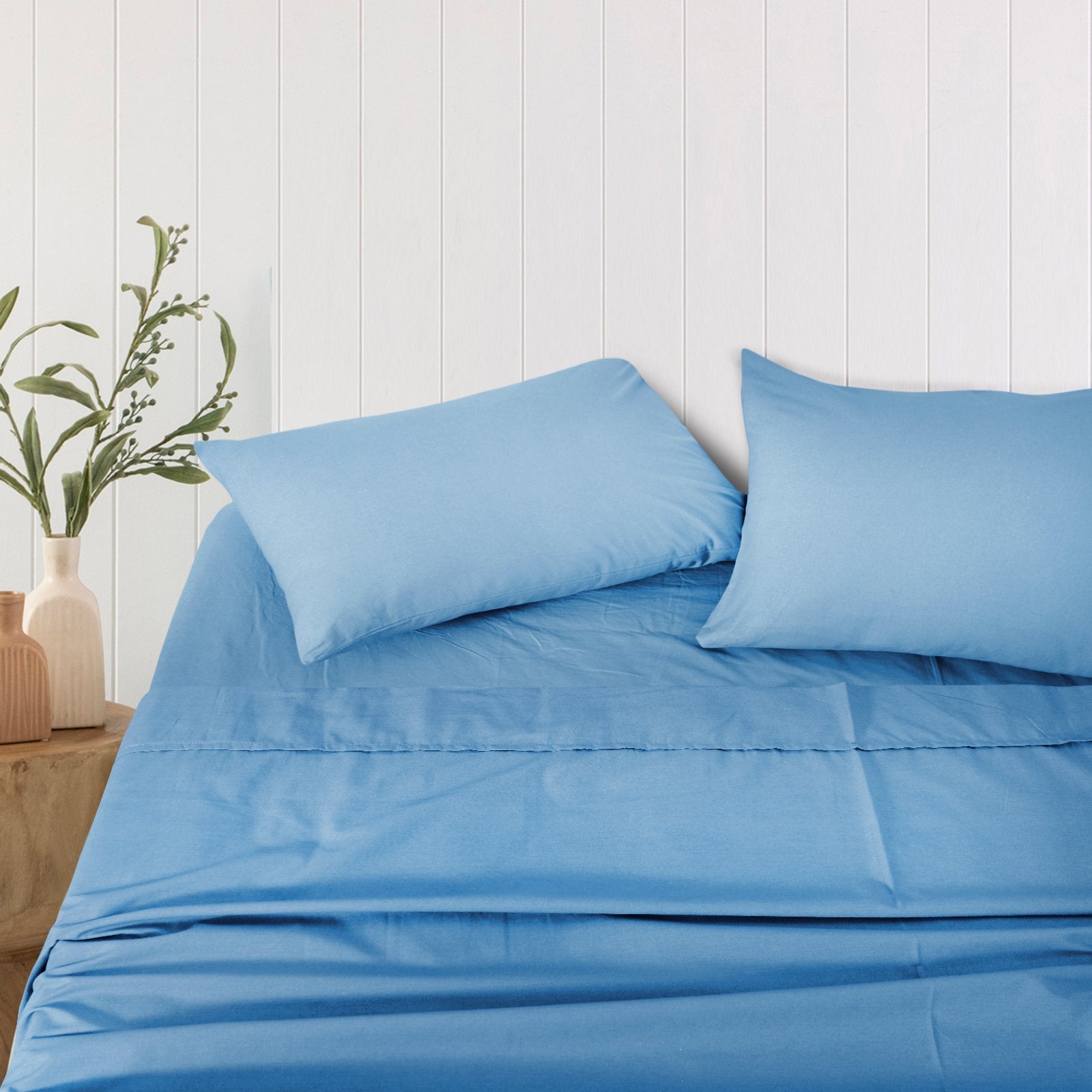 Pair of solid blue bamboo pillowcases propped neatly on a bed against a white wood-paneled wall