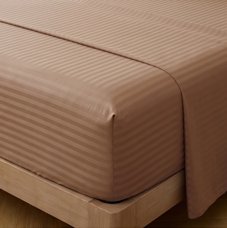Fitted corner of a brown satin stripe sheet neatly tucked over the edge of a mattress