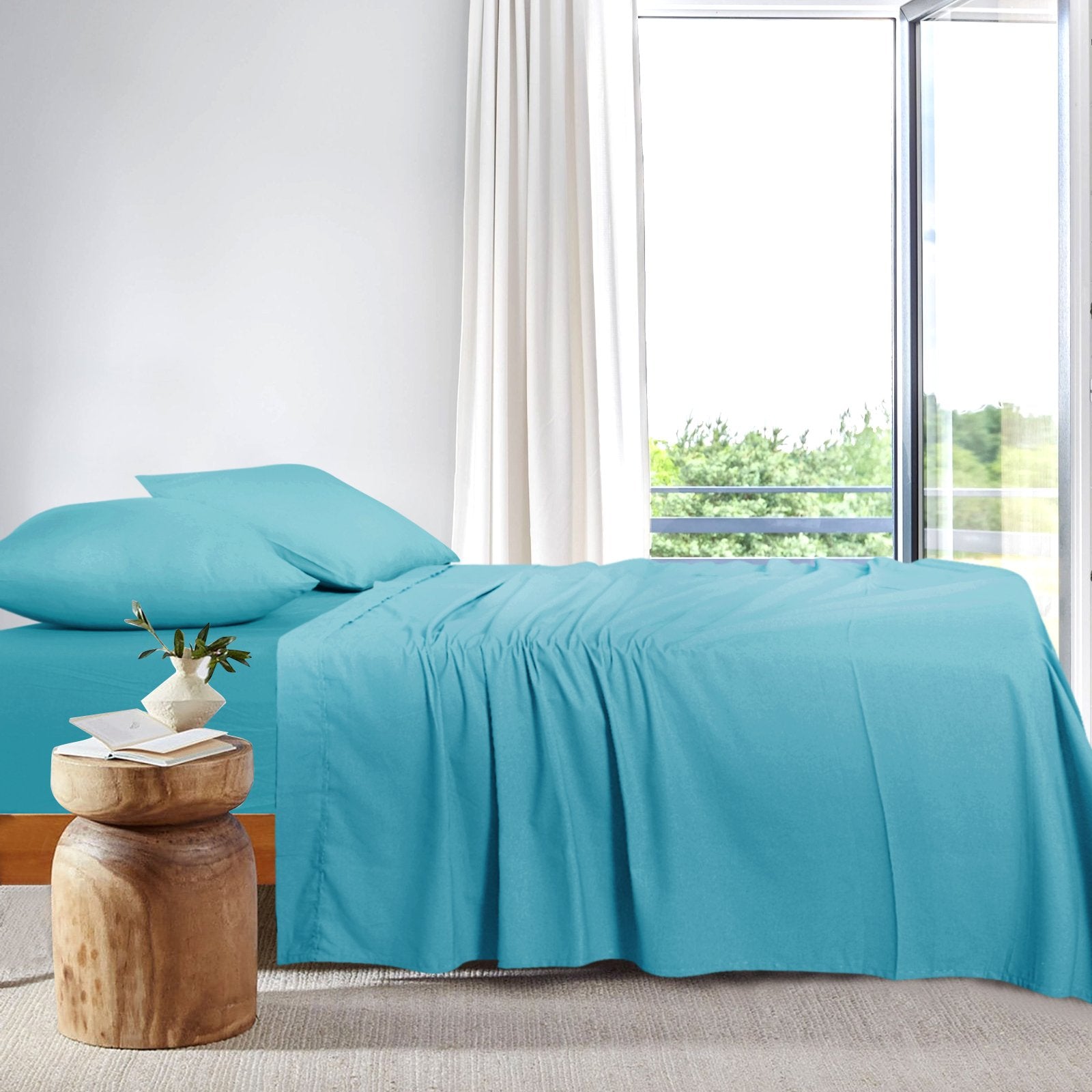 Side view of a modern platform bed neatly dressed in teal bamboo sheets positioned next to a large window