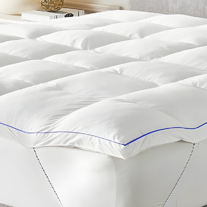 Full view of a plush white quilted mattress topper with blue edge piping on a mattress in an elegant bedroom