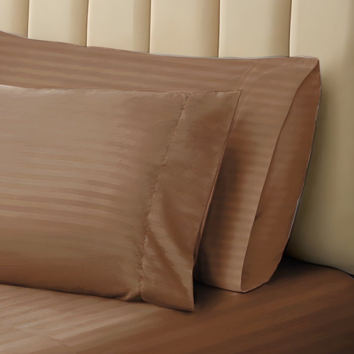 Pair of brown striped pillowcases propped neatly against a neutral tufted headboard