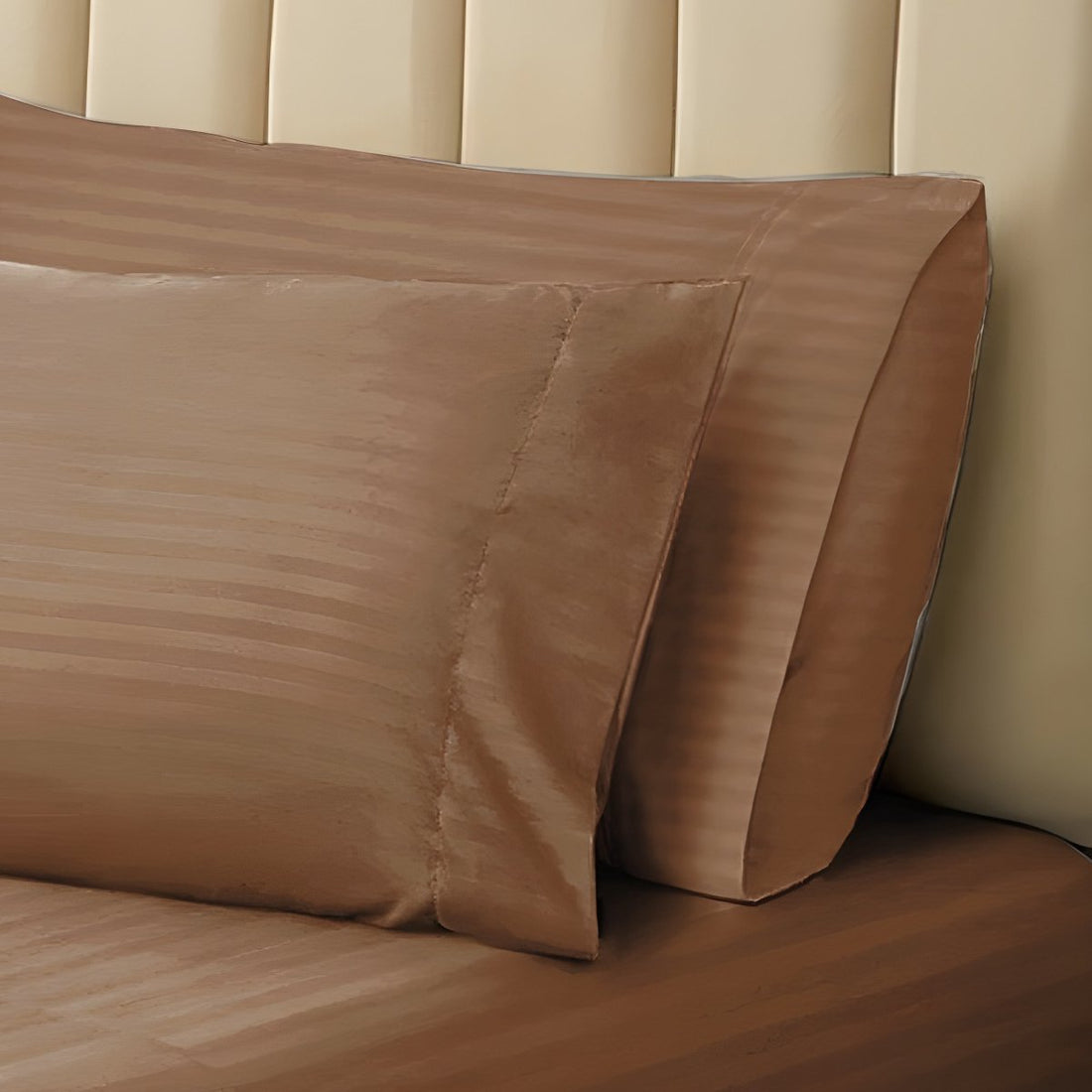 Pair of brown striped pillowcases propped neatly against a neutral tufted headboard