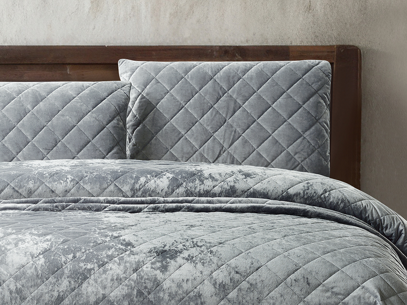 Silver grey velvet bedding with matching diamond-patterned pillows on a wooden bed.