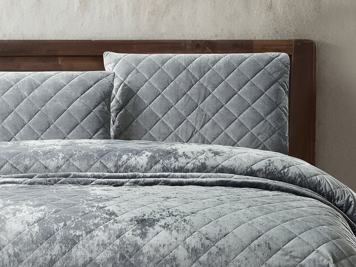 Silver grey velvet bedding with matching diamond-patterned pillows on a wooden bed.