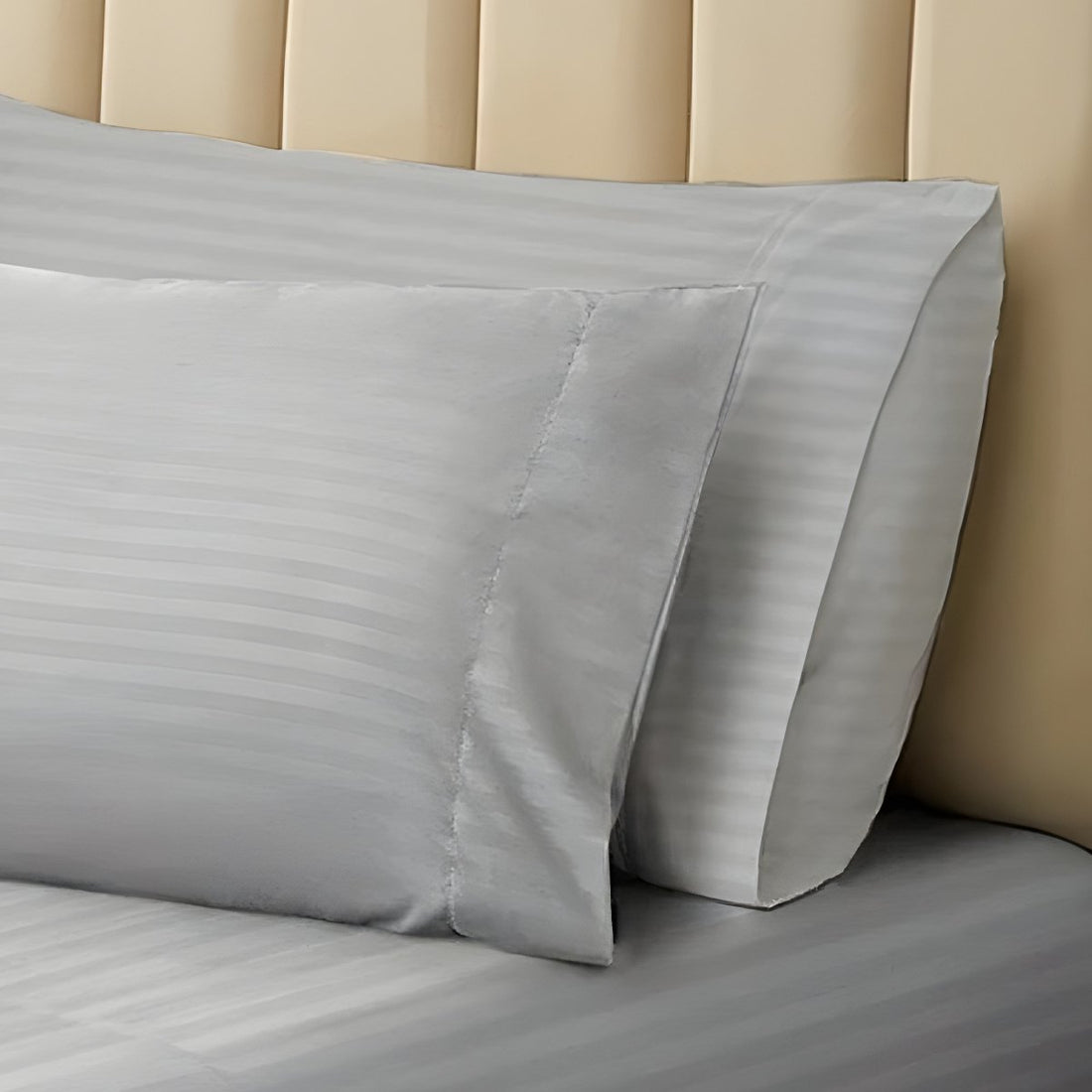 Pair of silver gray striped pillowcases resting against an upholstered neutral headboard