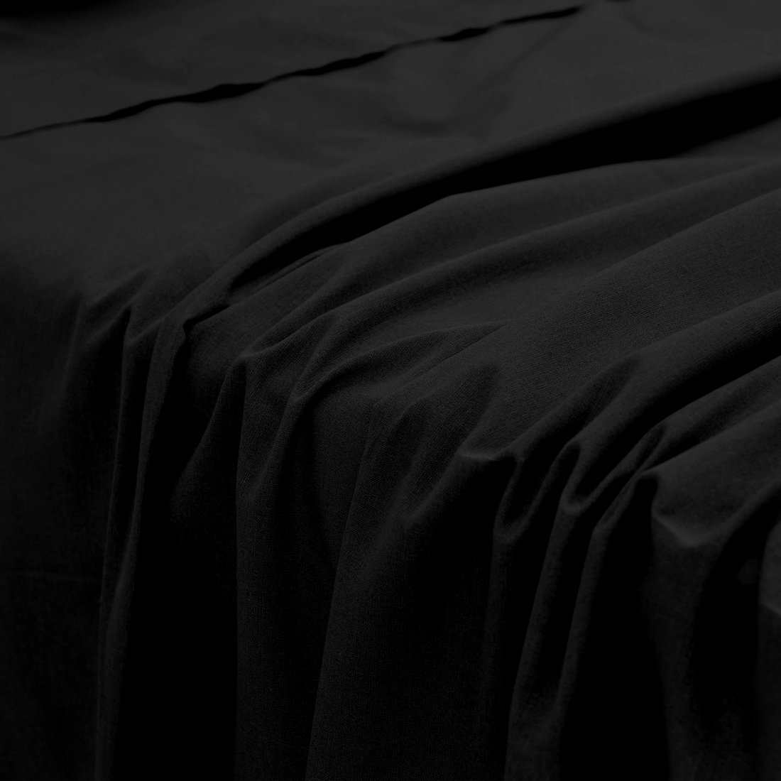 Close-up perspective of the smooth, soft fabric folds of a black bamboo fitted bed sheet