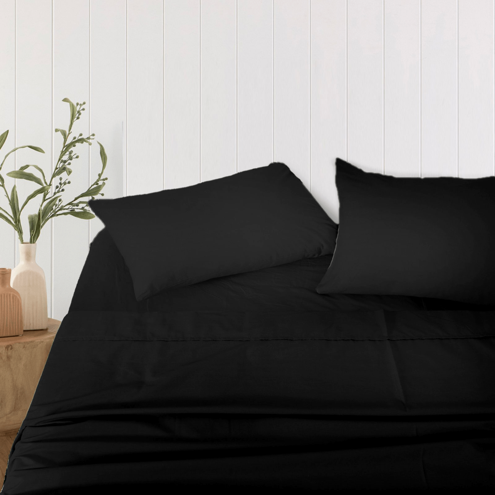 Pair of black bamboo pillowcases resting on a made bed against a white wood-paneled wall