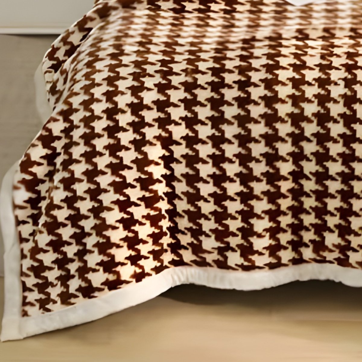 Close-up perspective of a warm brown houndstooth fleece blanket folded with a white pom-pom accent pillow