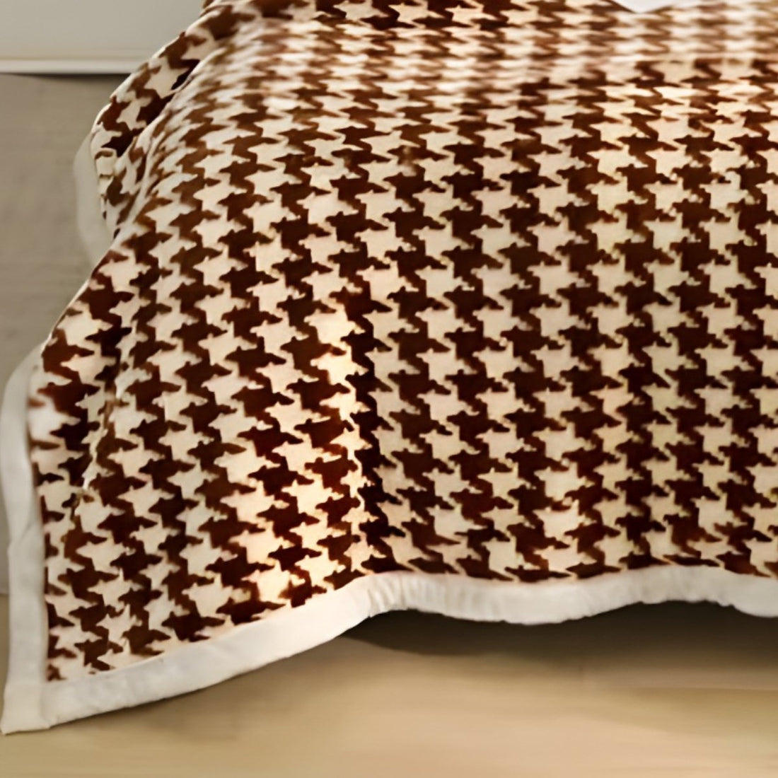 Close-up perspective of a warm brown houndstooth fleece blanket folded with a white pom-pom accent pillow