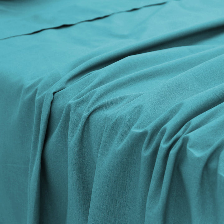 Close-up perspective of the smooth, silky fabric folds and texture of a teal bamboo bed sheet.