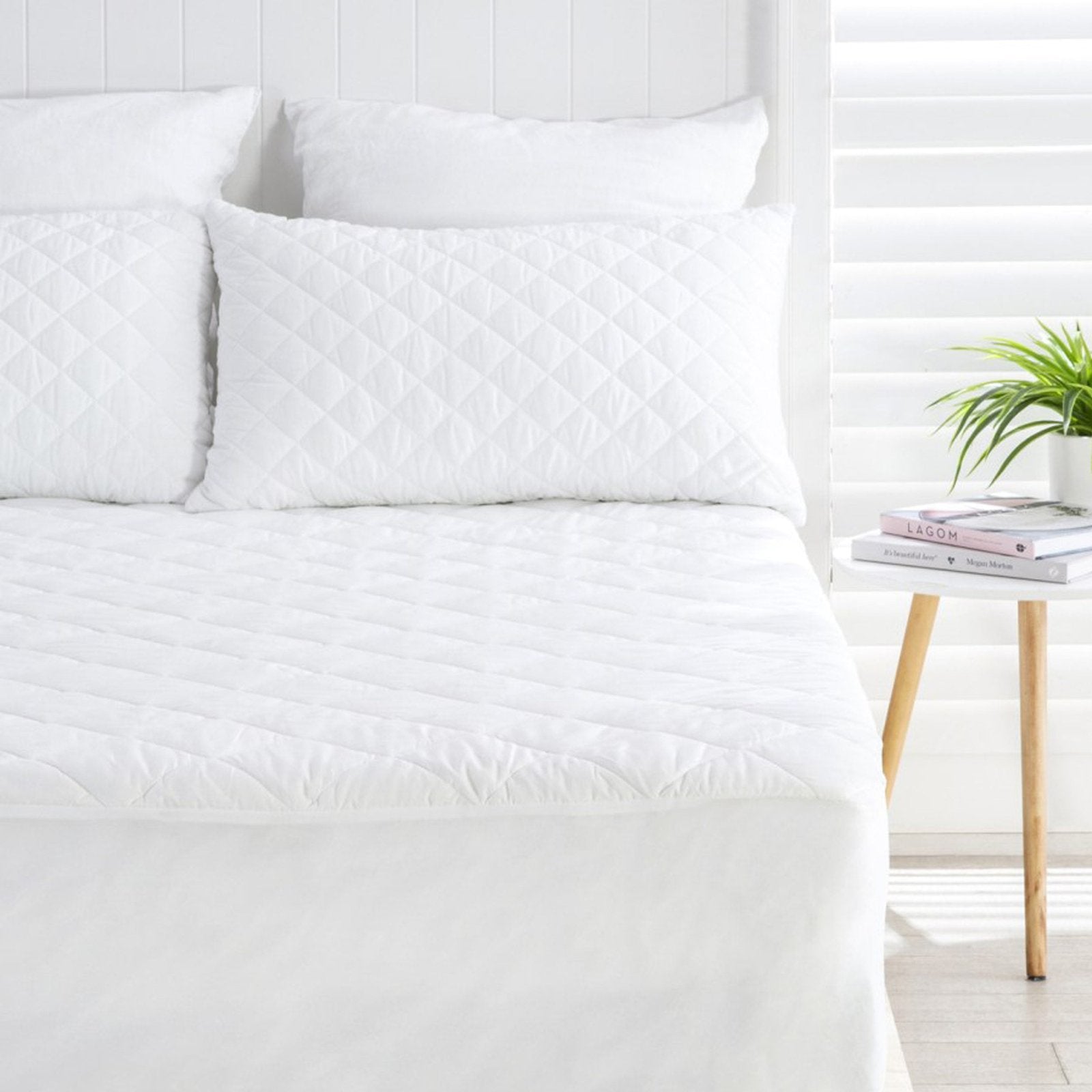 Water resistant quilted white mattress protector set shown with matching diamond-stitched pillows on a fully made bed