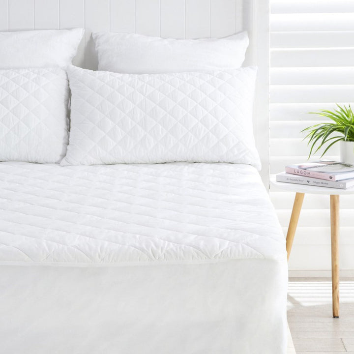 Water resistant quilted white mattress protector set shown with matching diamond-stitched pillows on a fully made bed