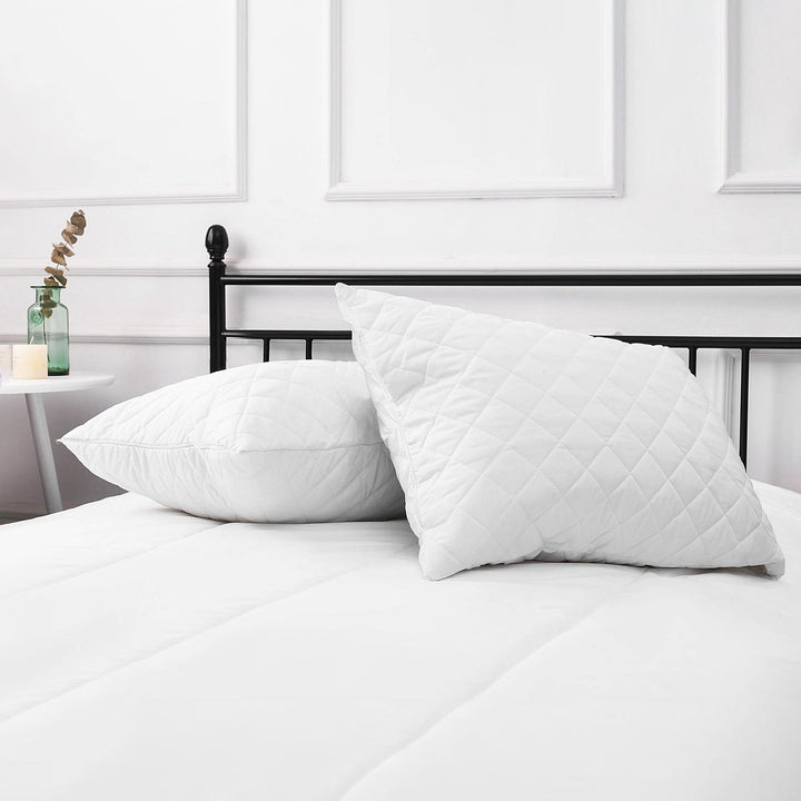 Set of two white water resistant quilted pillow protectors displayed upright on a made bed with a black headboard