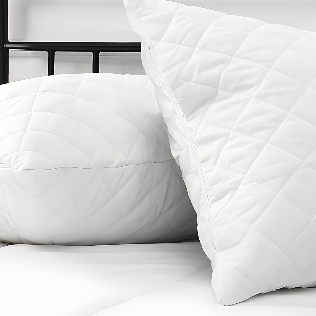 Close-up perspective of two white diamond-stitched quilted pillow protectors arranged on a mattress.