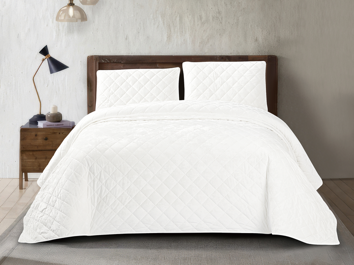 White crushed velvet bedspread set with diamond quilted detailing and matching pillows on a modern bed.