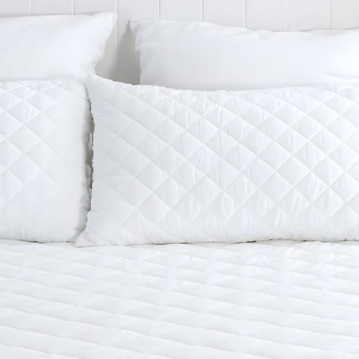 Full view of a white diamond quilted mattress protector styled neatly in a bright, modern bedroom