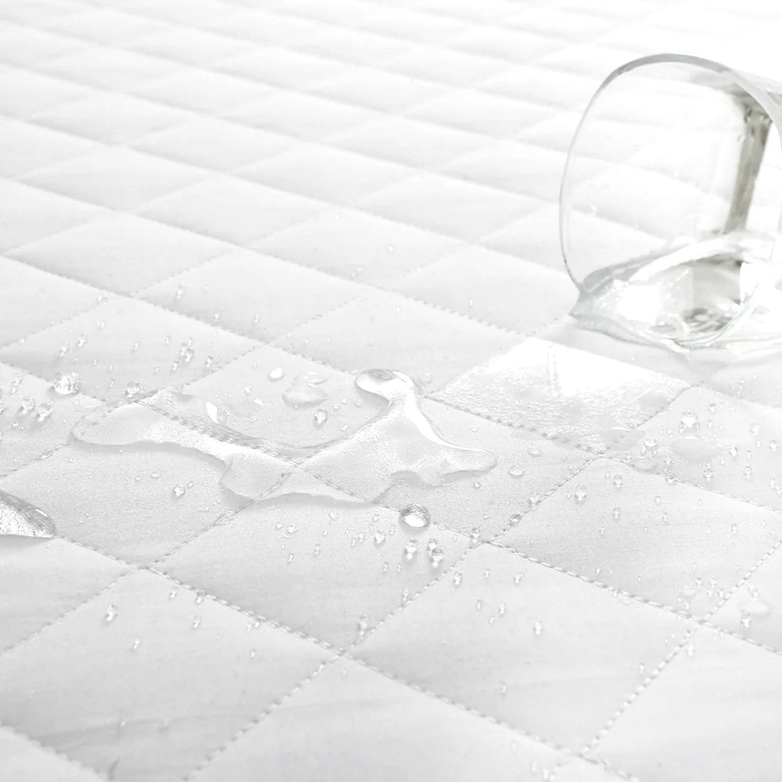 Water droplets beading on the surface of a white diamond quilted pillow protector demonstrating water resistance