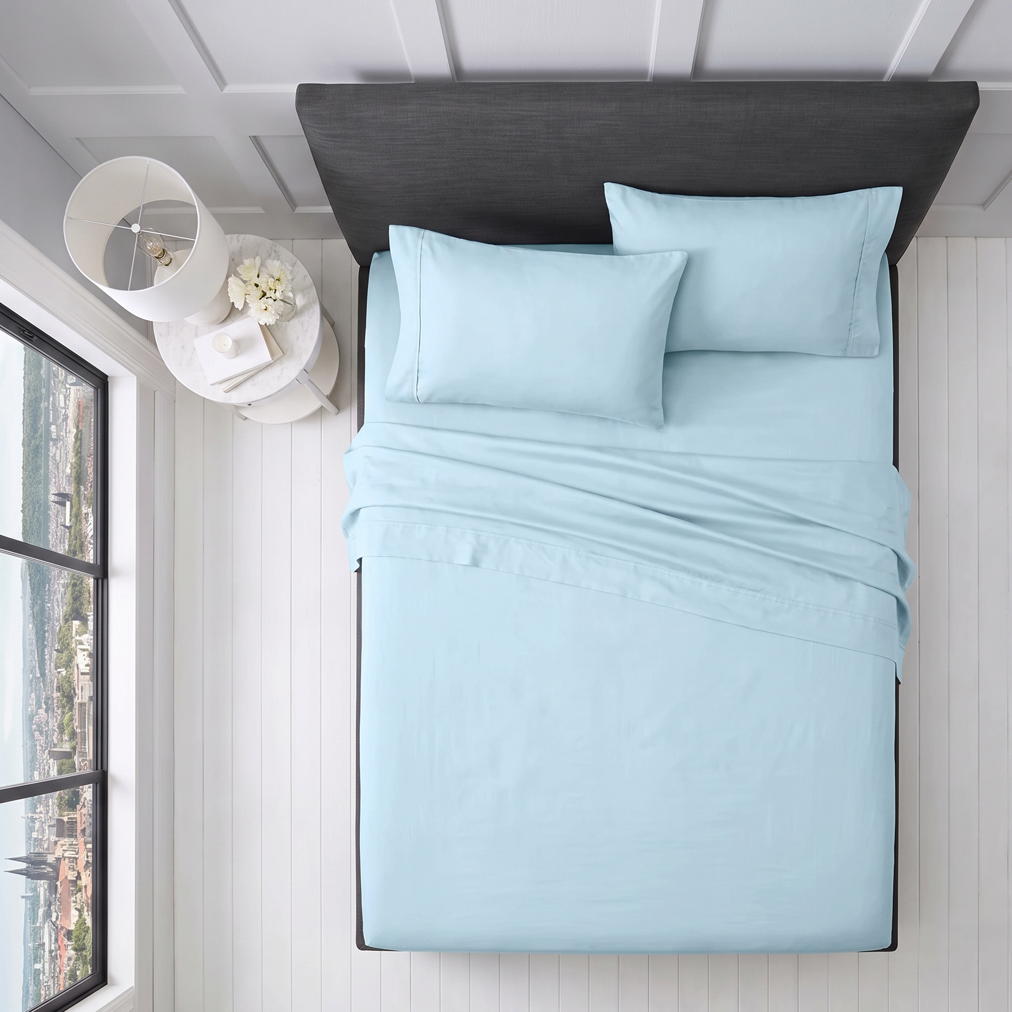 Neatly arranged light blue pillows and folded sheets on a grey upholstered bed