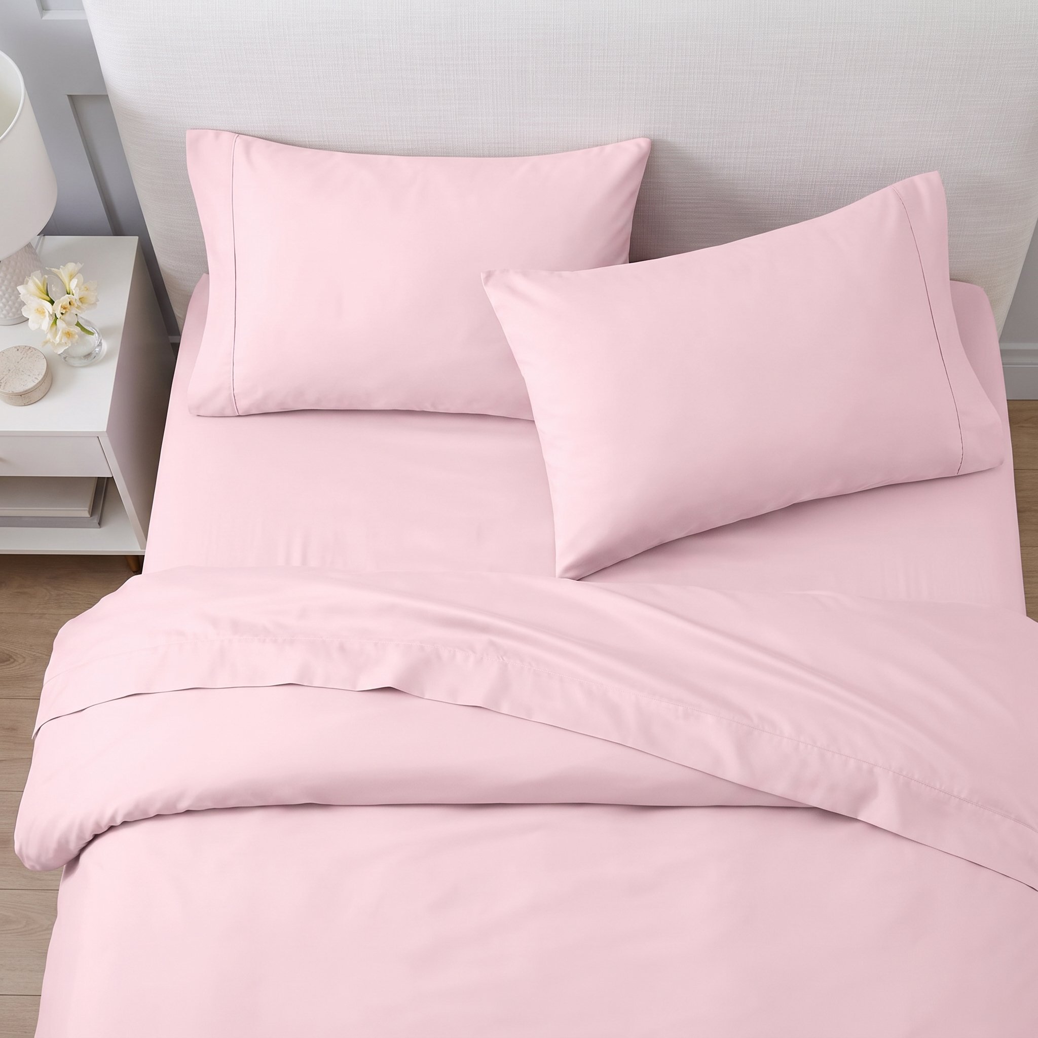 Neatly arranged blush pink pillows and folded sheets on a beige upholstered bed