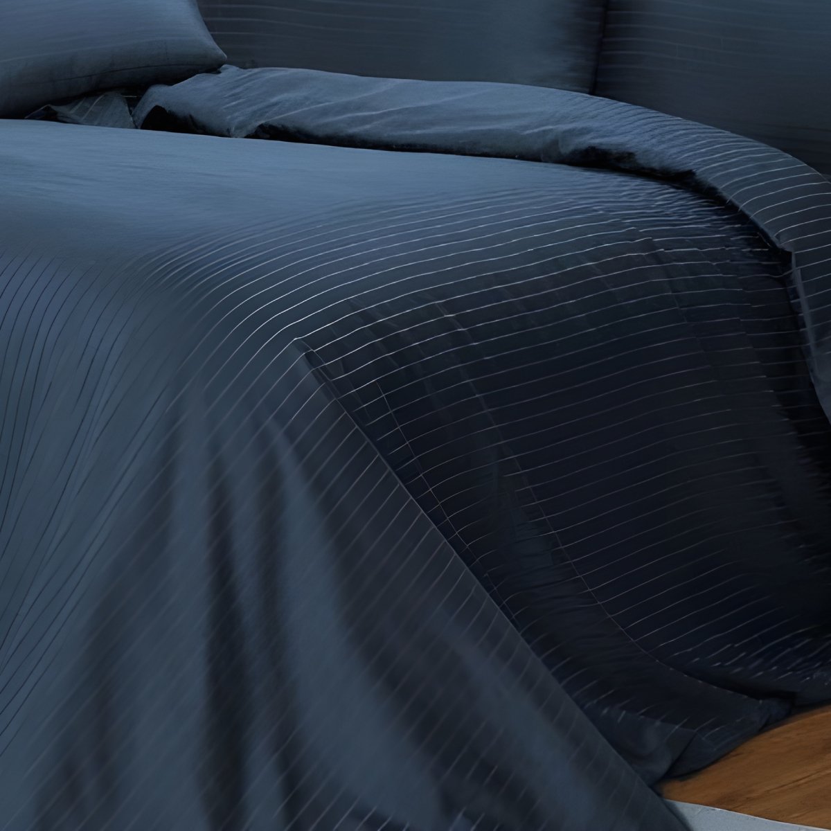 Side perspective of textured navy hotel stripe duvet cover draped over a mattress