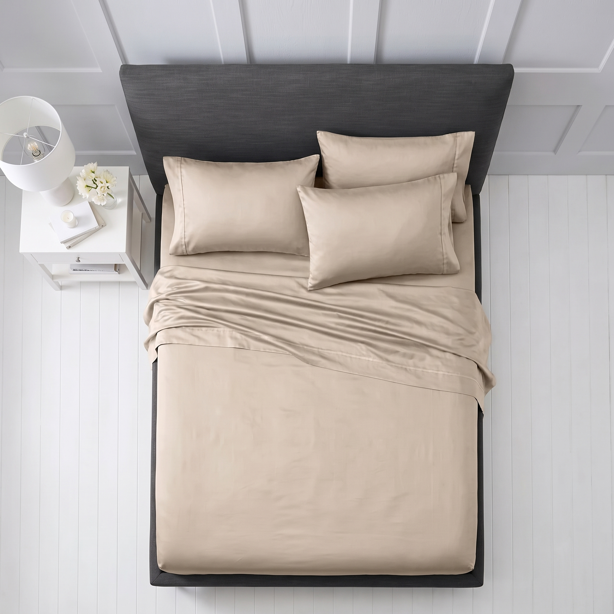 Neatly arranged beige pillows and folded sheets on a grey upholstered bed