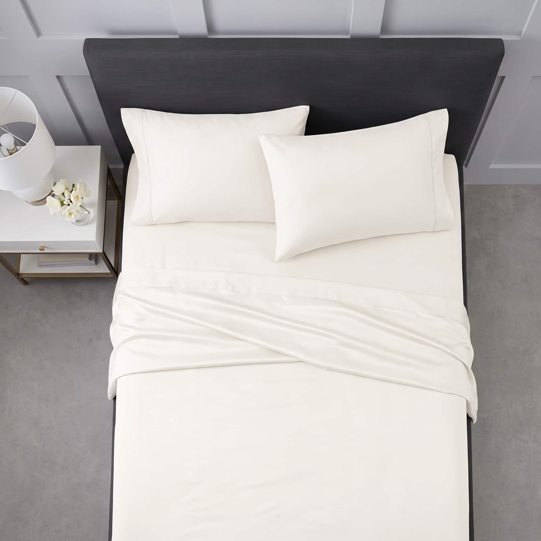 Neatly arranged cream pillows and folded sheets on a grey upholstered bed