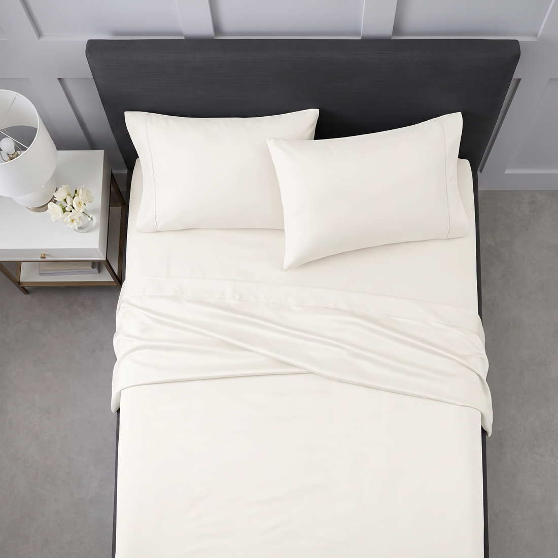 Neatly arranged cream pillows and folded sheets on a grey upholstered bed