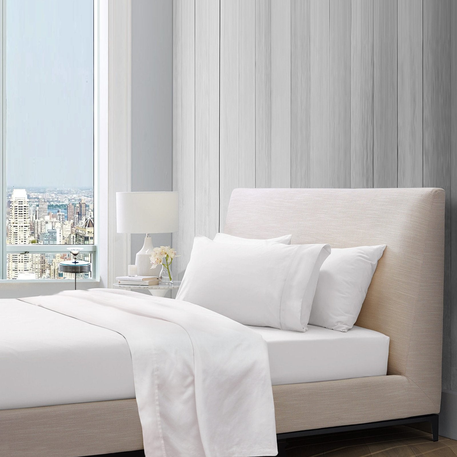 Plain white cotton sheet set styled on a bed with pillows in a bright bedroom