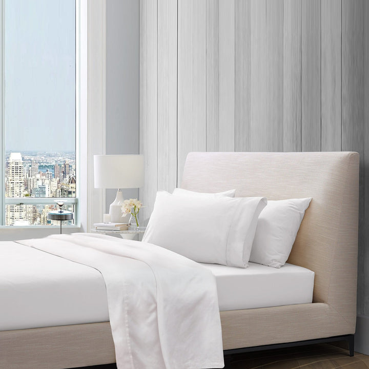 Plain white cotton sheet set styled on a bed with pillows in a bright bedroom