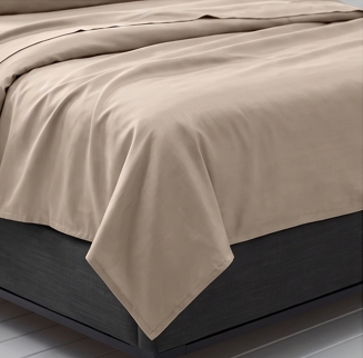 King size beige sheet set draped over a bed near a window with city view
