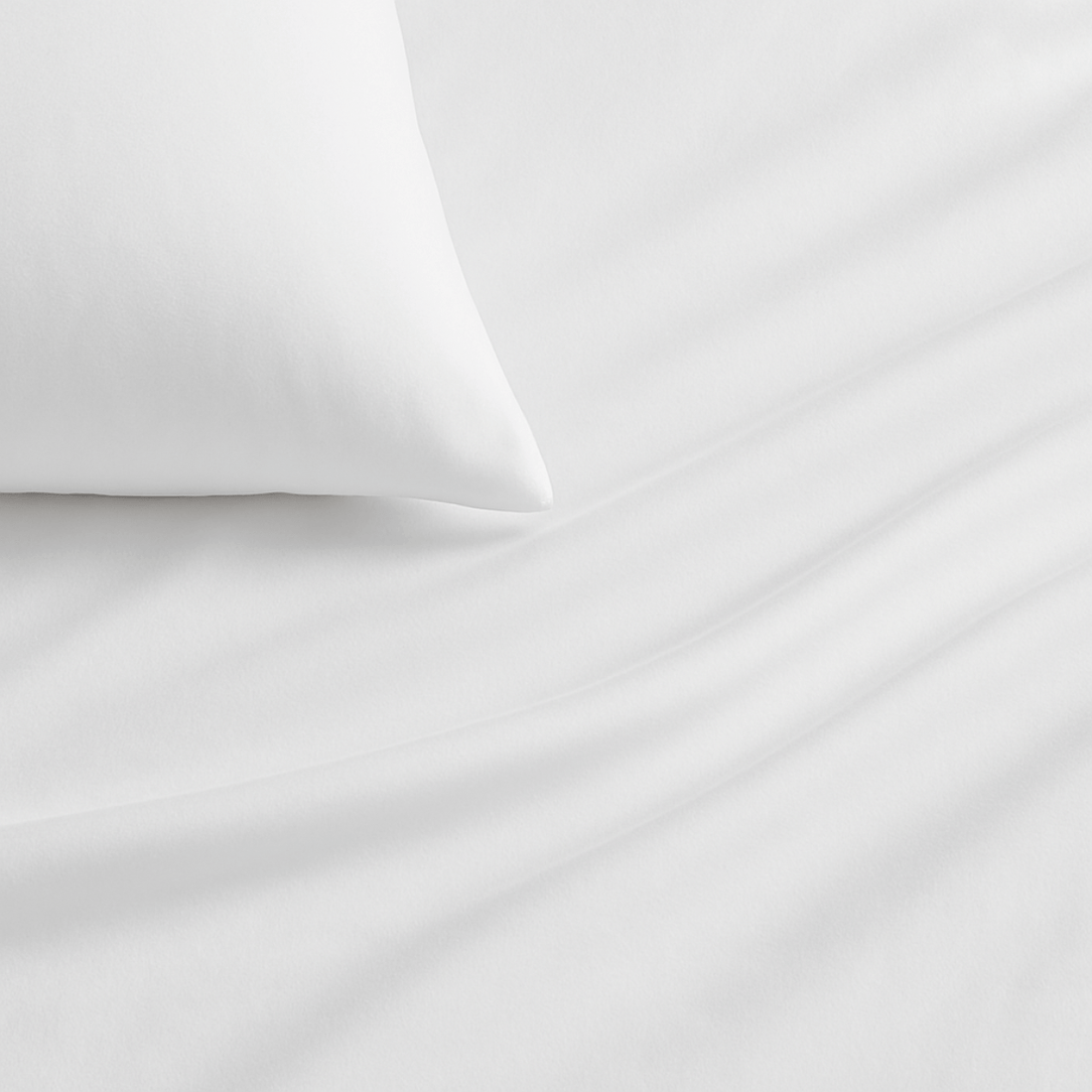 White bed sheets draped over a bed with pillows near a window