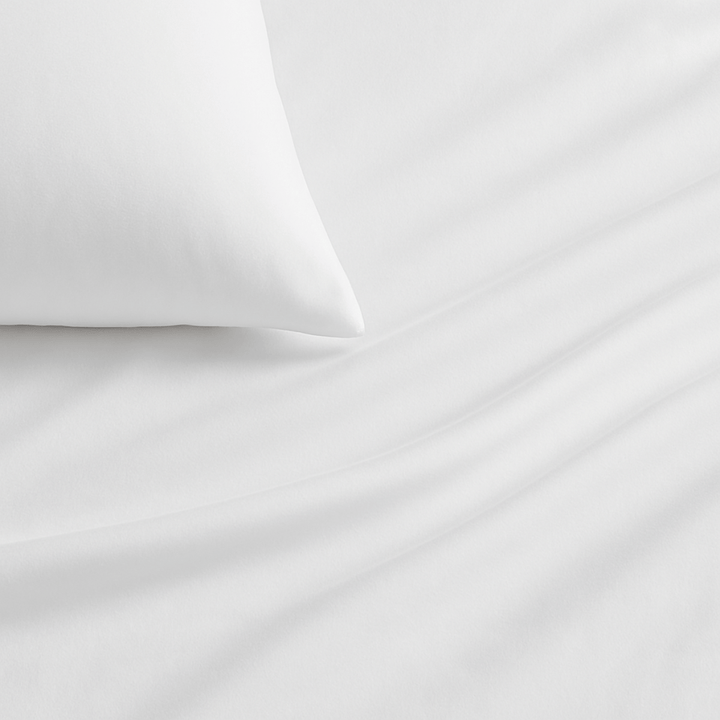 White bed sheets draped over a bed with pillows near a window